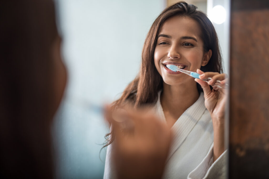 Portrait of beaming pretty woman brushing teeth while looking at mirror